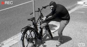A thief wearing a hoodie stealing a bicycle, caught in the act of cutting the bike lock with bolt cutters, in an urban street setting